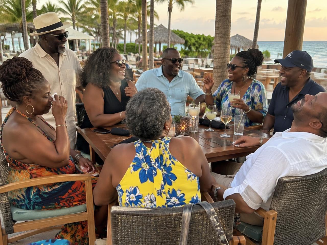 Black college friends in their 50s laughing together over drinks at a tropical resort table